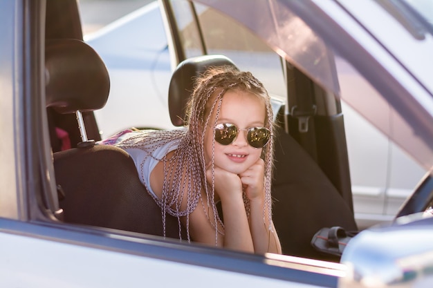 Lächelndes Teenager-Mädchen mit Afro-Zöpfen sitzt an einem heißen Sommertag im Fahrgastraum eines Autos. Ausflug