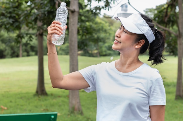 Lächelndes trinkendes Süßwasser der älteren Asiatin im Sommer am Park.