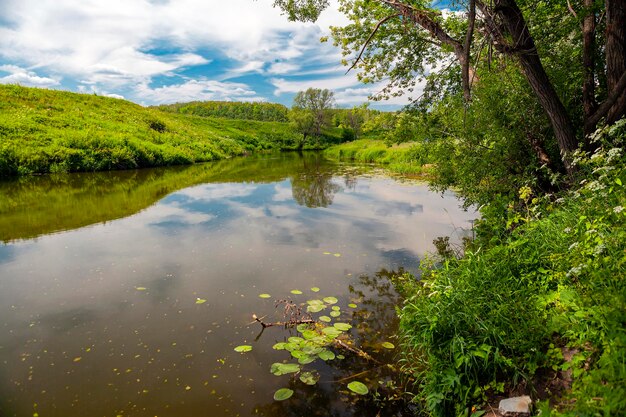 Ländliche Landschaft an einem Sommertag am Flussufer mit einer Reflexion des blauen Himmels. Russland.