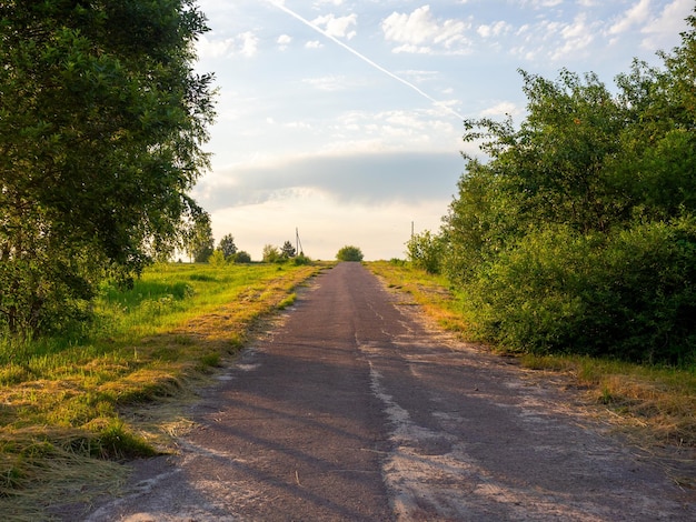 Ländliche Landschaft. Die Asphaltstraße geht bergauf, Wolken, Grün an den Straßenrändern. Sommer, Morgendämmerung