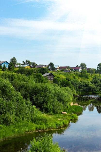 Ländliche Sommerlandschaft des russischen Norddorfes mit Holzhäusern nahe Fluss