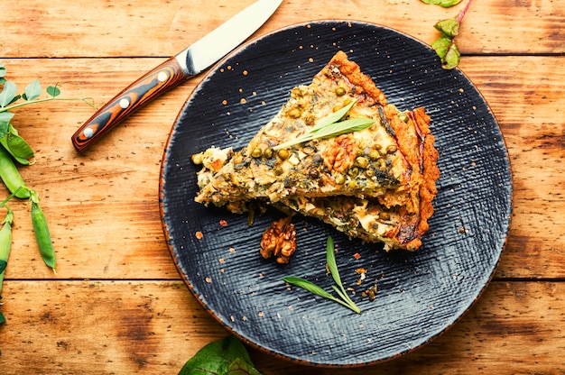 Ländlicher Kuchen mit Mangold, Feta und grünen Erbsen. Kuchen mit Kräutern auf rustikalem Holzhintergrund