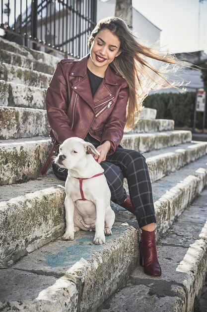 Foto länge voller lächelnder junger frau mit einem hund, der auf den stufen sitzt