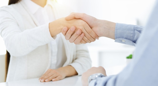 Lässig gekleideter Geschäftsmann und Frau, die sich nach der Vertragsunterzeichnung im sonnigen Büro die Hände schütteln Handshake-Konzept