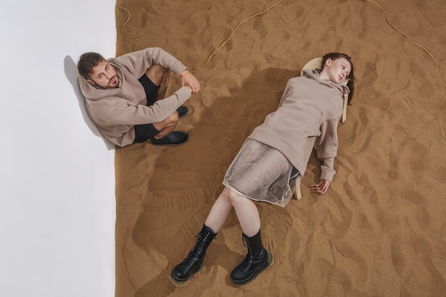 Lässig gekleideter Mann und Frau, die voneinander entfremdet sind und auf dem Sandhintergrund posieren.