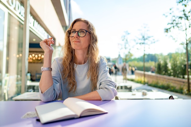 Lässige frau, die am tisch sitzt und notizen im notizbuch auf der caféterrasse macht