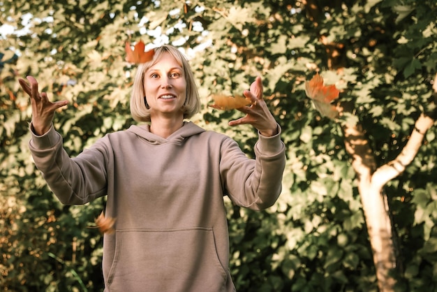 Lässige, fröhliche Frau, die Spaß daran hat, Blätter im Herbst im Stadtpark zu werfen