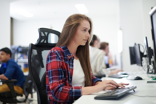 Lässige Geschäftsfrau, die an einem Desktop-Computer in einem modernen Großraum-Startup-Büro arbeitet