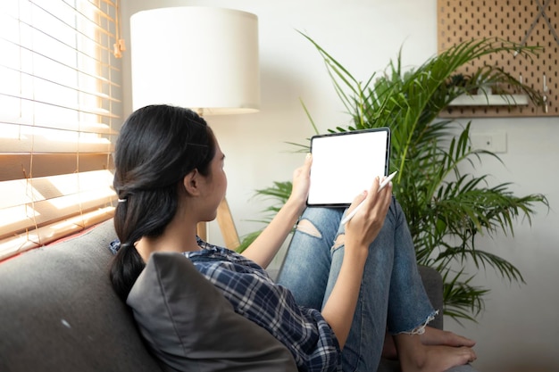 Lässige junge Frau, die auf der Couch sitzt und ein digitales Tablet verwendet