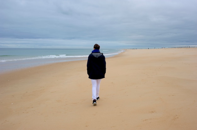 Lässige junge Frau geht an einem wolkigen Tag am Strand entlang