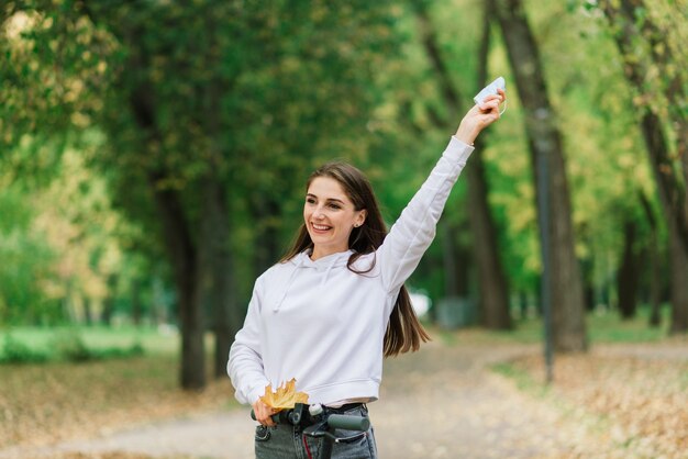 Lässige kaukasische Frau, die schützende Gesichtsmaske trägt, die städtischen Elektroroller im Stadtpark während der Covid-Pandemie reitet. Konzept der städtischen Mobilität.