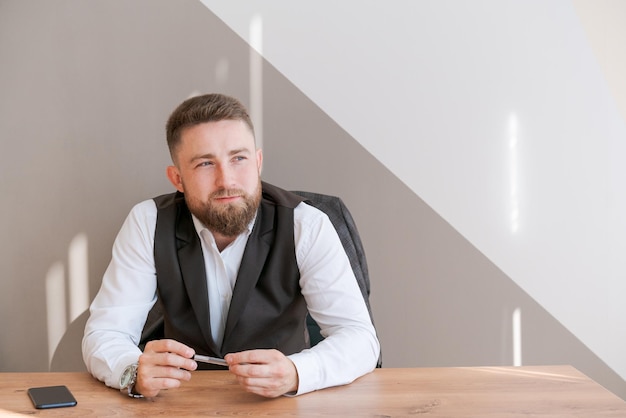 Lässiger bärtiger Geschäftsmann, der mit Stift in der Hand am Tisch sitzt und denkt