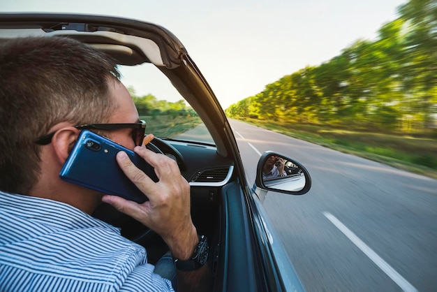 Lässiger Geschäftsmann, der auf Handy spricht, während er Auto-Seitenansicht fährt Hübscher junger Mann im Hemd, der auf Handy spricht, während er Lenkradfokus auf Rückspiegel hält