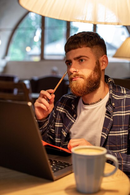 Lässiger Geschäftsmann oder Freiberufler, der seine Arbeit am Notebook plant und an einem Laptop mit Smart...