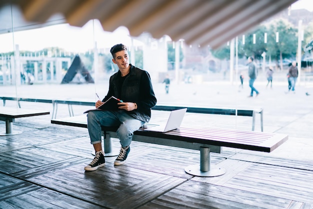 Lässiger Hipster-Mann mit Notizbuch auf Bank sitzend