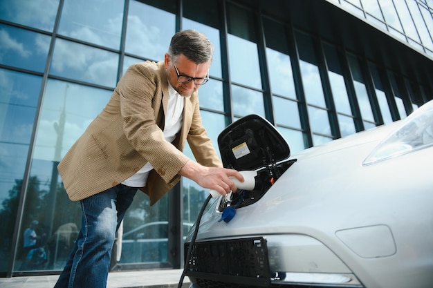 Lässiger Mann in der Nähe von Elektroautos, der auf das Ende des Batterieladevorgangs wartet