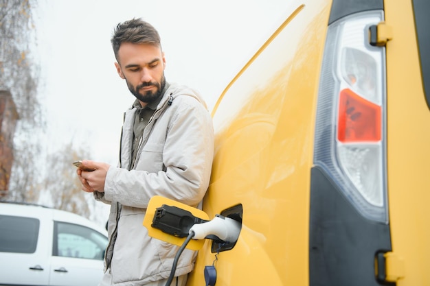 Lässiger Mann in der Nähe von Elektroautos, der auf das Ende des Batterieladevorgangs wartet