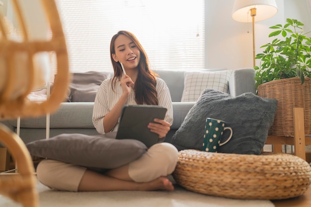 Lässiges arbeiten zu hause entspannen lässig mit tablet-gerät im wohnzimmerasiatische weibliche erwachsene handeingabe suchen oder sms über laptop sofa arbeiten von zu hause aus mit glück friedlich lächelnden ideen konzept