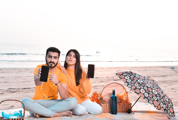 lässiges glückliches paar, das celphone am strand zeigt indisches pakistanisches modell