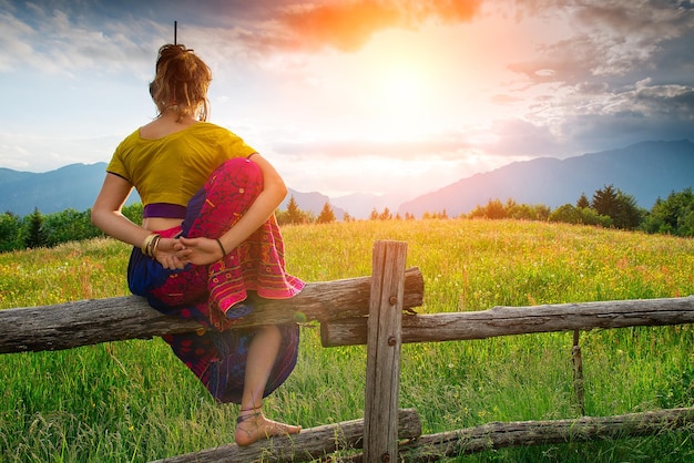 Lässiges Mädchen entspannt sich beim Stretching und Yoga allein in den Bergen über einem Zaun auf einer wunderschönen Frühlingswiese