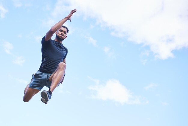 Läufer springt und Himmel mit Platz für Wolkenmodelle und Fitness in der Natur, Action und Freiheit. Sportler im niedrigen Winkel und im Freien für Workout-Übungen und Training mit schnellen Bewegungen für die Gesundheit