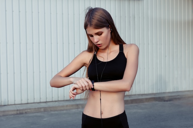 Läuferin, die sich nach dem Training in der Stadt ausruht. Fitnessfrau in Sportkleidung mit Kopfhörern, die Musik hören und lachend wegschauen.