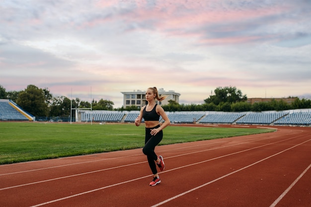 Läuferin im Sportbekleidungsjoggen, Training im Stadion. Frau macht Dehnübungen vor dem Laufen auf der Outdoor-Arena