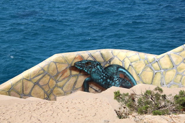 Un lagarto azul pintado en una roca con el océano al fondo