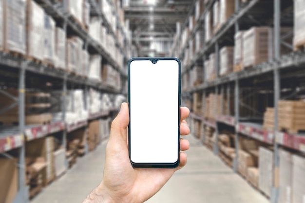 Lager mit einer Hand, die ein leeres Smartphone hält Verschwommenes Industrielager mit Waren und Produkten Logistik Business Delivery Services Konzept Foto in hoher Qualität