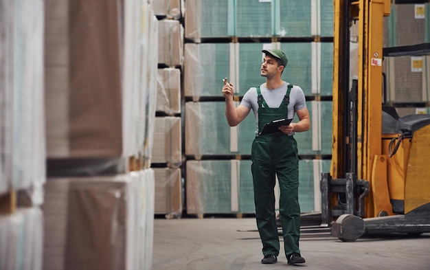 Foto lagerarbeiter in grüner uniform und notizbogen in den händen überprüft die produktion