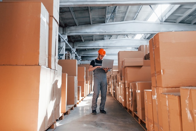 Lagerarbeiter in Uniform und modernem Laptop in Händen kontrolliert die Produktion.