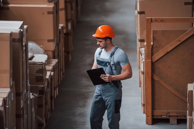 Lagerarbeiter in Uniform und Notizblock in Händen kontrolliert die Produktion.