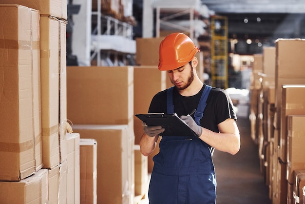 Lagerarbeiter in Uniform und Notizblock in Händen kontrolliert die Produktion.