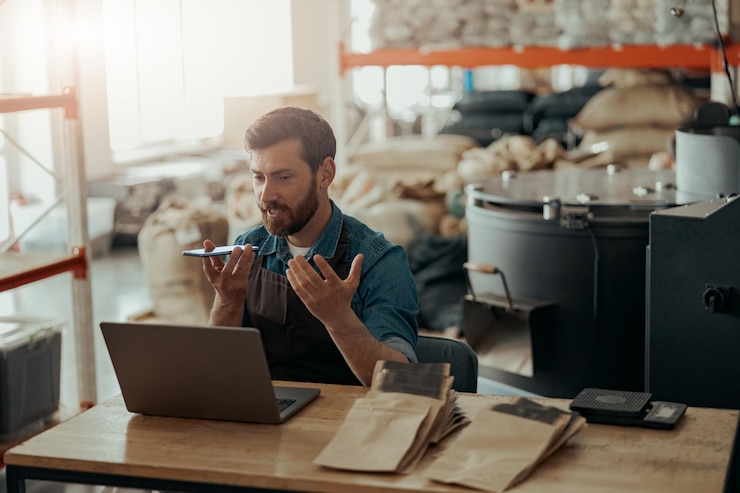 Foto lagerarbeiter zeichnen audionachrichten am telefon auf, die an einer kleinen kaffeefabrik arbeiten