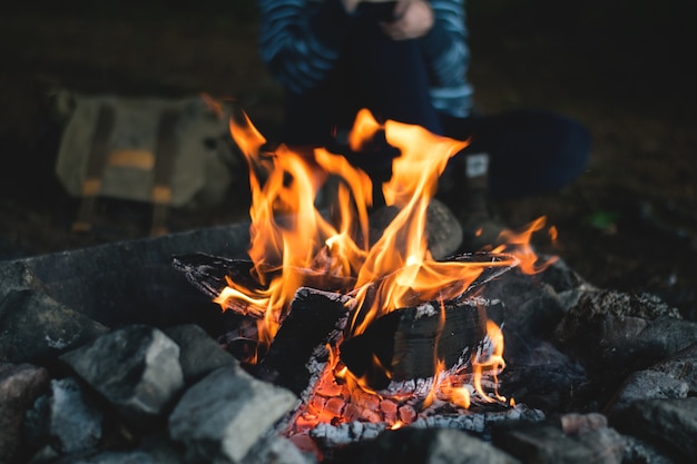 Lagerfeuer im Wald in der Dämmerung mit einer Person im Hintergrund