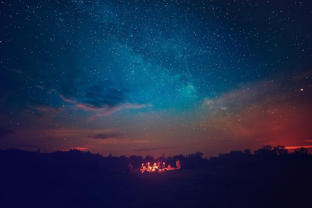 Lagerfeuer unter dem erstaunlichen blauen Sternenhimmel mit vielen leuchtenden Sternen und Wolken. Reisekonzept für Freizeitaktivitäten im Freien.