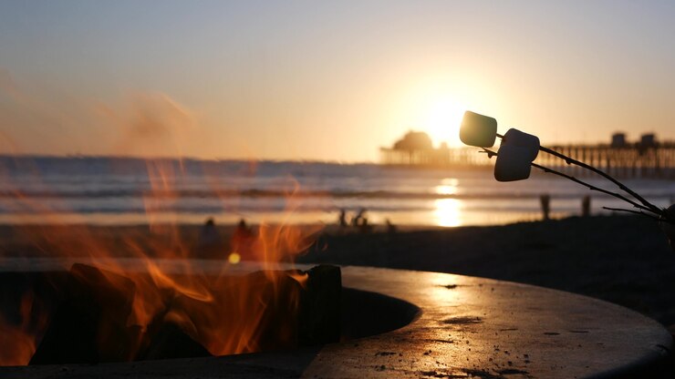 Foto lagerfeuerstelle von oceanside pier, kalifornien usa. lagerfeuer am meeresstrand, lagerfeuerflamme im zementring für grill, meerwasserwellen. marshmallow am stiel erhitzen, rösten oder rösten. romantischer sonnenuntergangshimmel