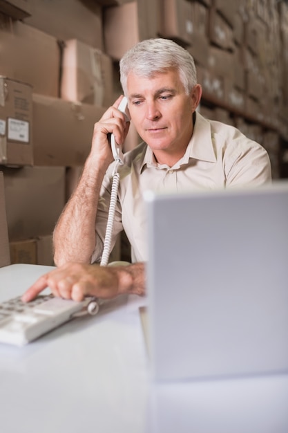 Lagerverwalter, der Telefon und Laptop verwendet