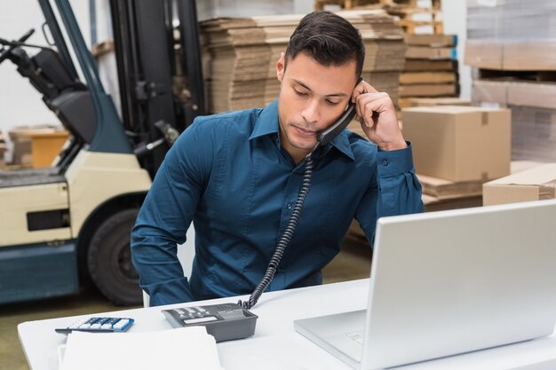 Lagerverwalter, der Telefon und Laptop verwendet