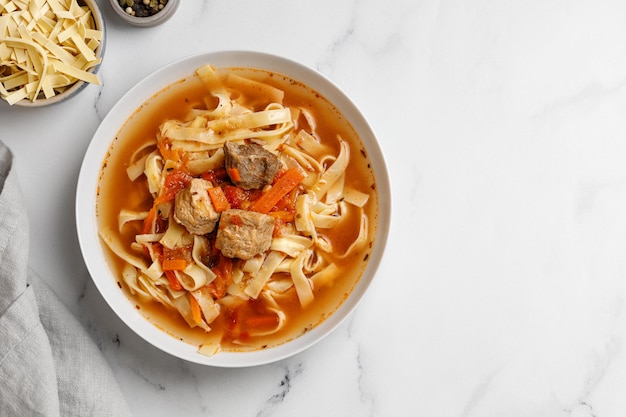 Lagman. La sopa uzbeka nacional con fideos y trozos de carne, verduras fritas. Vista superior. plato blanco y fondo blanco