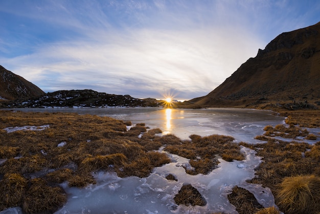 Lago alpino congelado de alta altitude, reflexões ao pôr do sol