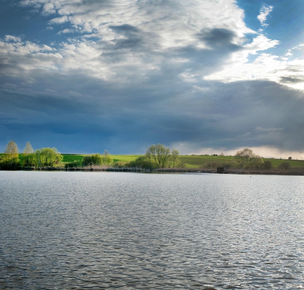 Lago antes da tempestade e árvores e campos lindamente iluminados na primavera, paisagens pitorescas