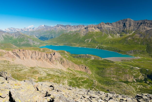 Lago azul de gran altitud, presa en los Alpes franceses italianos. Amplia vista desde arriba, claro cielo azul.