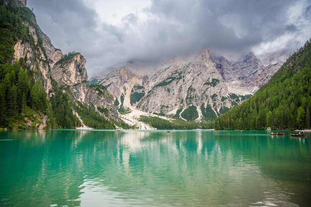 Lago Braies cercado por florestas de pinheiros e as cordilheiras rochosas das Dolomitas em um dia nublado na Itália