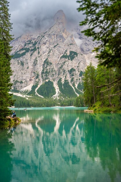 Foto el lago braies rodeado de bosques de pinos y las cordilleras rocosas de los dolomitas en un día nublado en italia