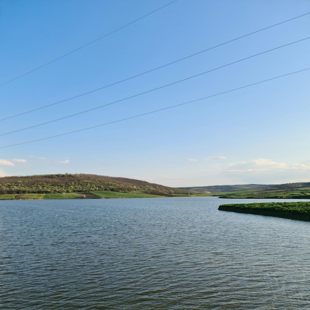 Un lago con una colina verde al fondo y un cielo azul con nubes.