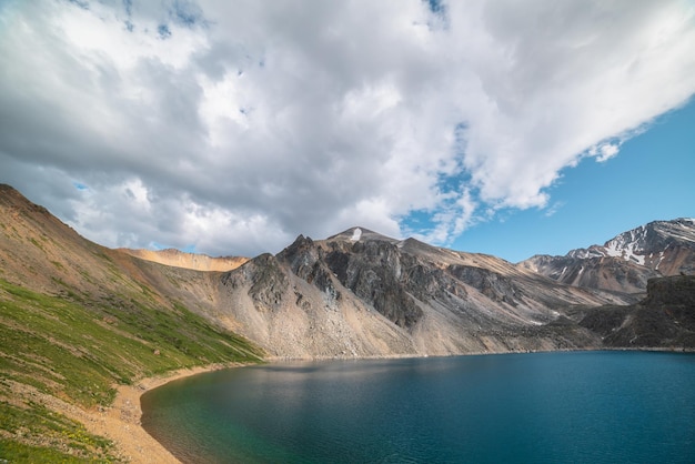 Lago de montanha profunda de cor azul fantasma entre montanhas altas com pico pontiagudo em clima mutável Maravilhosa vista dramática para o lago de montanha azul profundo entre rochas afiadas iluminadas pelo sol sob céu nublado