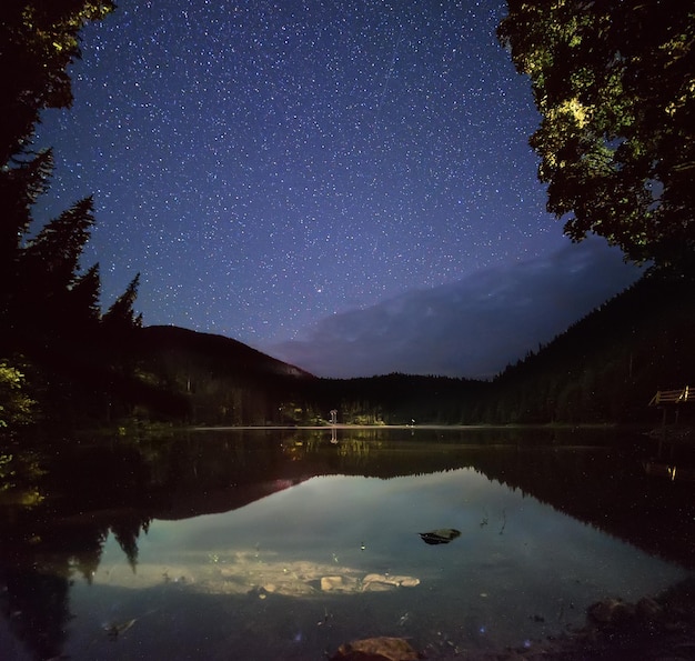 Lago de montanha Synevir à noite com céu estrelado e reflexos na água. Outddors naturais viajam em fundo escuro. Cárpatos, Ucrânia