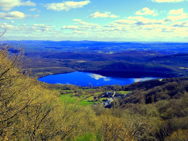 Un lago está rodeado de árboles y un cielo azul.