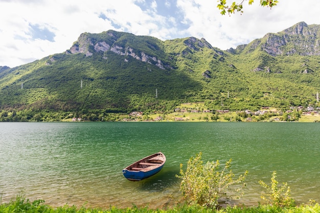 lago Idro Lago d'Idro contra el fondo de rocas con árboles de hoja perenne y un barco de pesca solitario